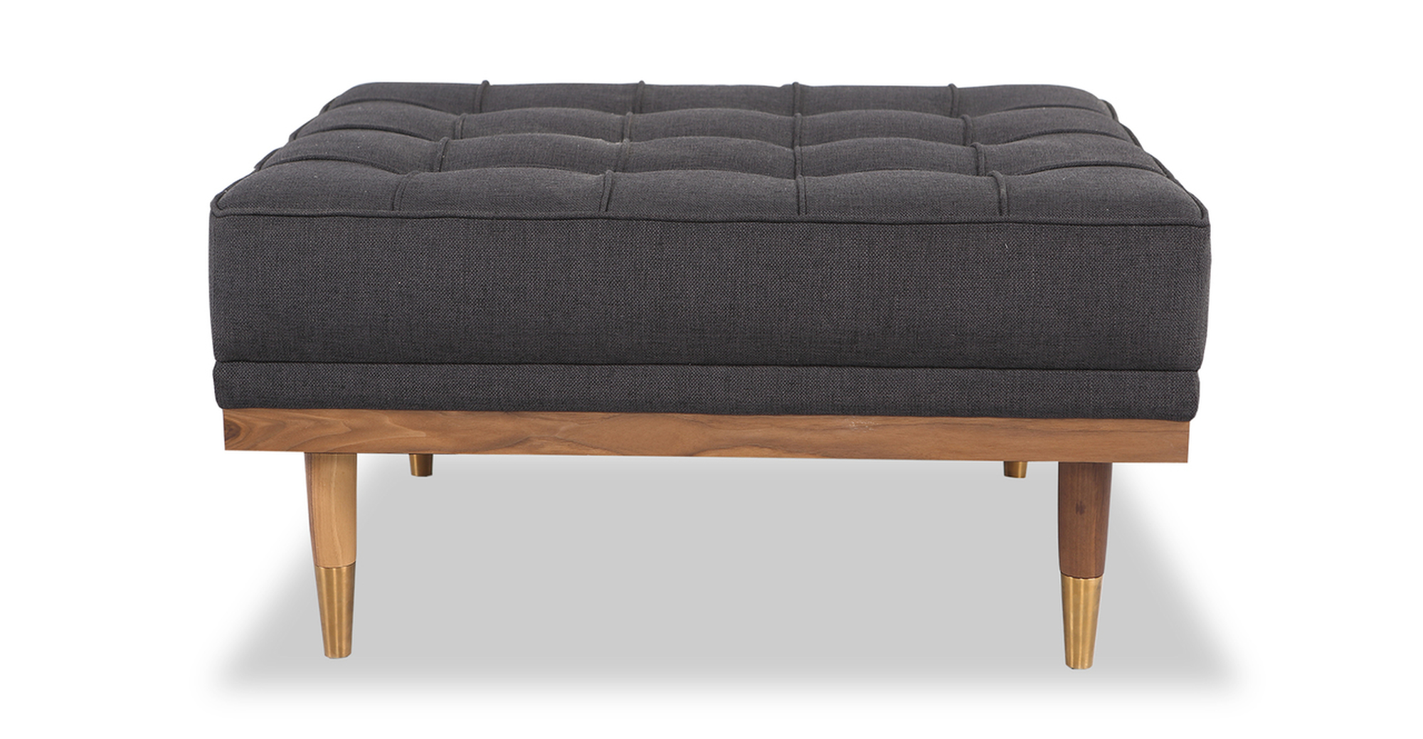 Woodrow ottoman in woven Ink. There is button tufting on the ottoman cushions. The frame and legs are walnut wood toned. The legs have brass colored ferrules on the ends. The upholstery color is dark grey.