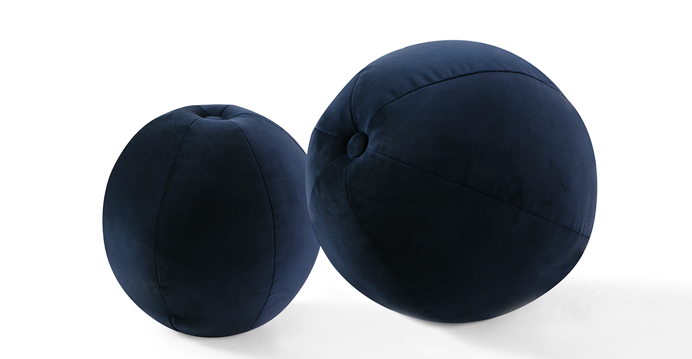 Set of two round ball pillows, one larger and one smaller. The ball has a button at center and uses several areas of stitching to create the tight ball shape.